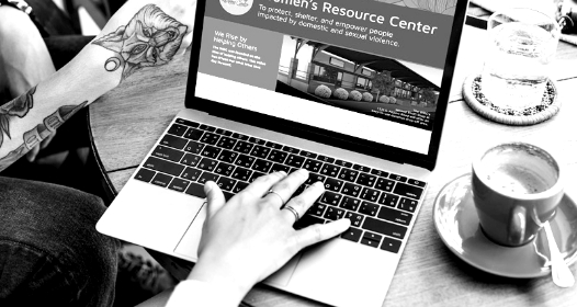 A woman works on a laptop with a cup of coffee to the right of her computer.