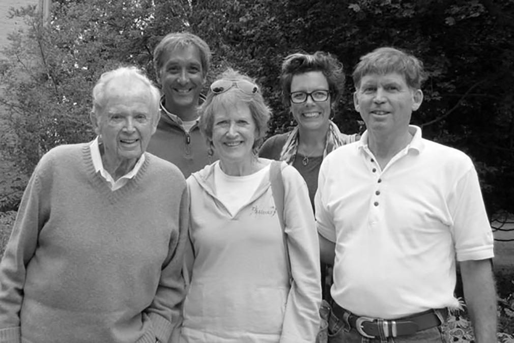 Five people stand together in front of trees while smiling.