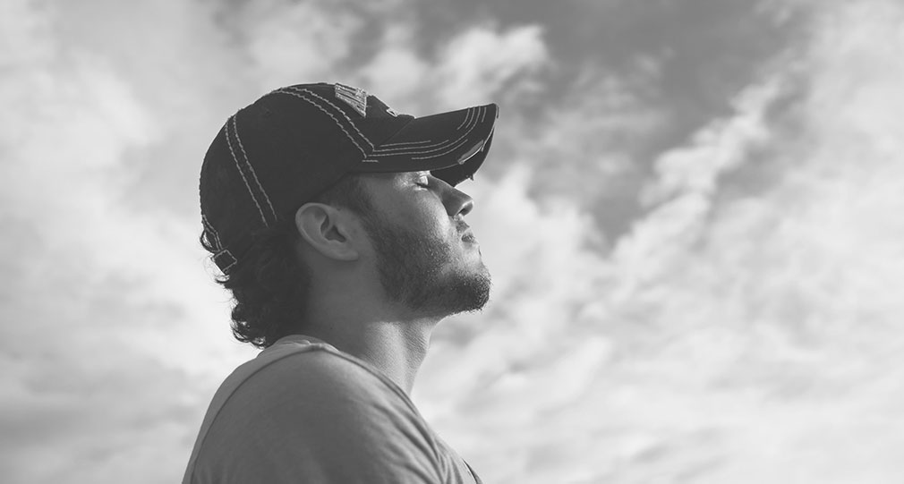 A man wearing a baseball hat turns his face to the sun with his eyes closed.